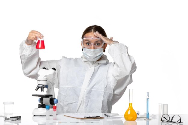 防護服を着た正面図の女性医師と白い背景の赤い溶液でフラスコを保持しているマスクcovidウイルスパンデミックコロナウイルス