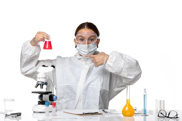 Front view female doctor in protective suit and with mask holding flask with red solution on white background covid virus pandemic coronavirus