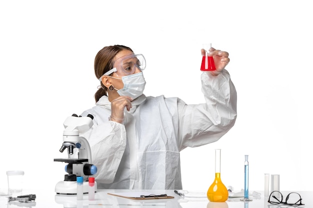 Вид спереди женщина-врач в защитном костюме и с маской, держащей фляжку с красным раствором на белом столе, вирус пандемии коронавируса
