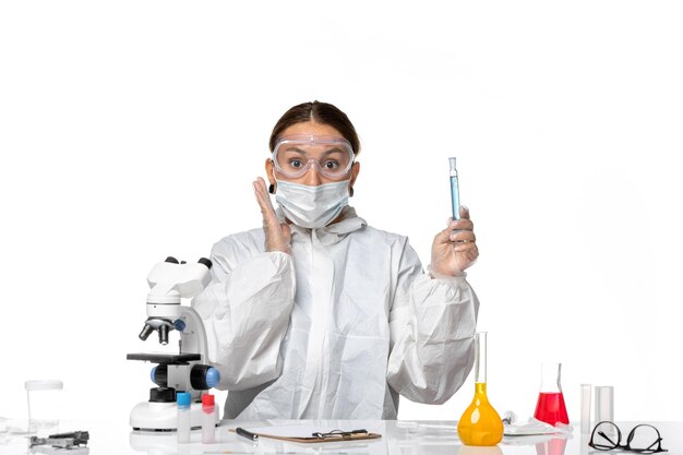 Front view female doctor in protective suit and with mask holding flask with solution on light-white background covid- pandemic virus coronavirus