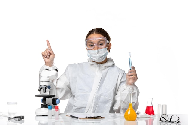 Front view female doctor in protective suit and with mask holding flask with solution on the white background covid pandemic virus coronavirus