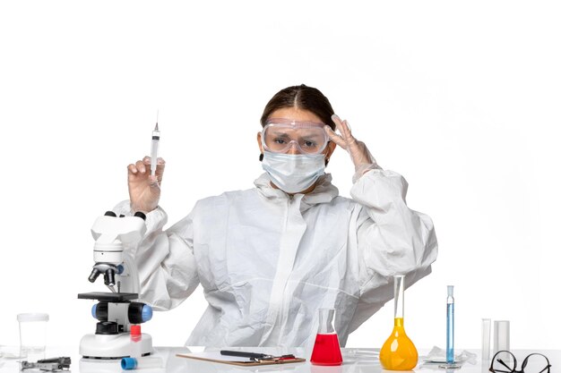 Front view female doctor in protective suit and with mask holding injection on light-white background virus medicine covid pandemic