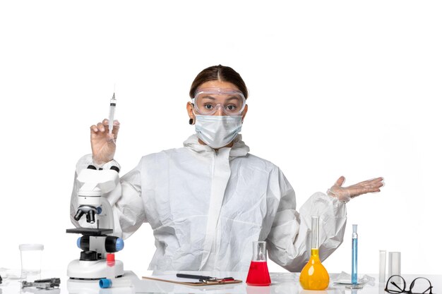 保護スーツを着て、白い背景に注射を保持しているマスクを持つ女性医師の正面図ウイルス薬covidパンデミック