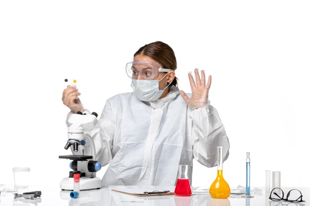 Front view female doctor in protective suit and with mask holding little samples on light-white background medicine health pandemic virus coronavirus