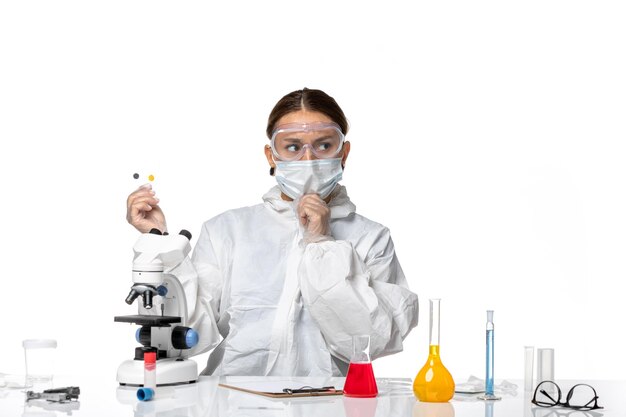 Вид спереди женщина-врач в защитном костюме и с маской, держащая маленькие образцы на белом фоне, медицина, пандемический вирус, коронавирус