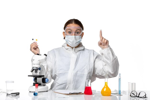 防護服を着た正面図の女性医師と白い背景の薬の健康パンデミックウイルスコロナウイルスの小さなサンプルを保持しているマスク