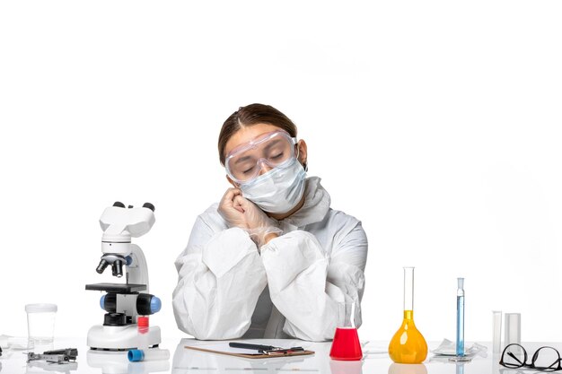 Front view female doctor in protective suit and with mask sitting with solutions on light white background virus medicine covid health pandemic