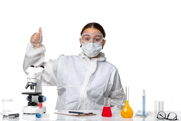 Front view female doctor in protective suit and with mask sitting with solutions posing on white background virus covid- health pandemic