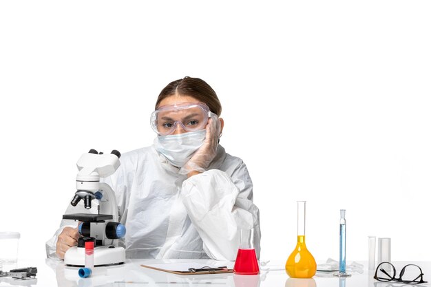 Front view female doctor in protective suit and with mask sitting with solutions on the white background pandemic virus coronavirus covid health