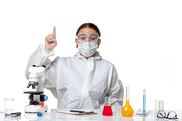 Front view female doctor in protective suit and with mask sitting with solutions on white background virus covid- health pandemic