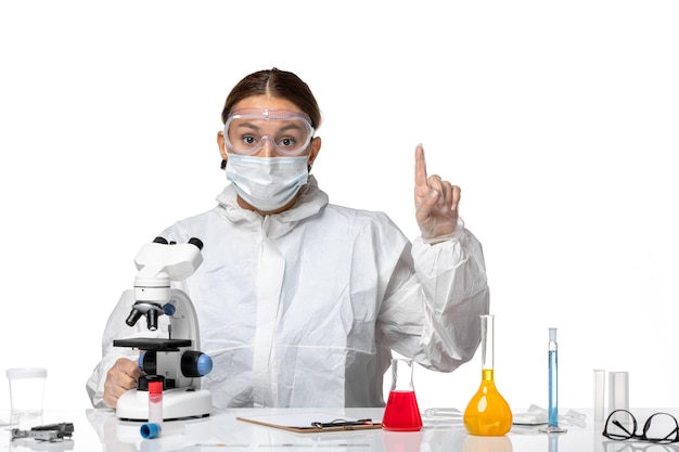 Front view female doctor in protective suit and with mask using her microscope on white background health pandemic virus coronavirus