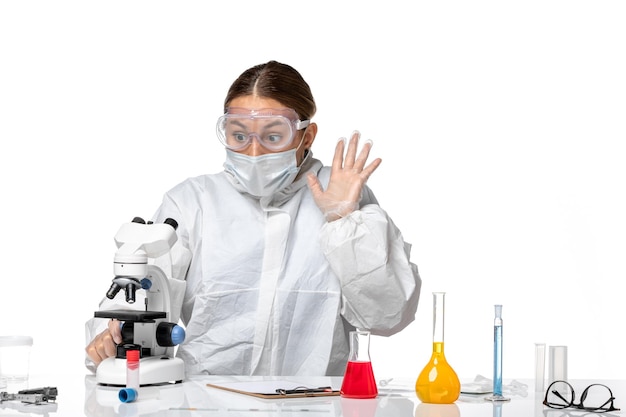 Вид спереди женщина-врач в защитном костюме и с маской с помощью микроскопа на светлом белом фоне пандемический вирус здоровья коронавирус