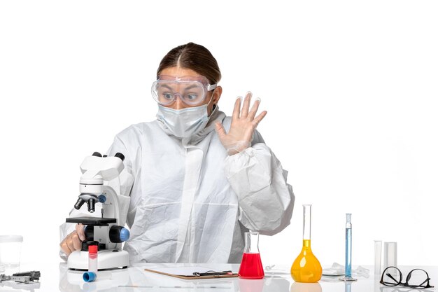 보호 복과 밝은 흰색 배경에 현미경을 사용하는 마스크가있는 전면보기 여성 의사 건강 대유행 바이러스 코로나 바이러스