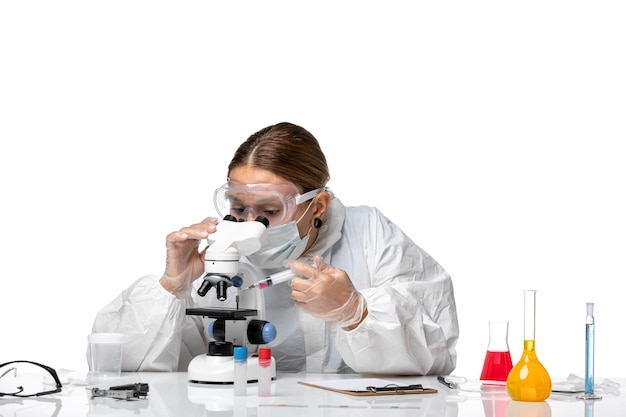 Вид спереди женщина-врач в защитном костюме и с маской с помощью микроскопа на белом фоне пандемического здоровья коронавируса вируса ковид