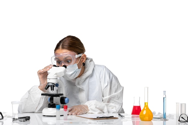 保護スーツと白い背景の上の顕微鏡を使用してマスクを使用して正面図の女性医師健康covidウイルスパンデミックコロナウイルス
