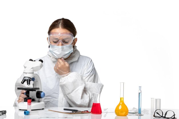 Front view female doctor in protective suit and with mask using microscope on a white background medicine covid- health pandemic virus