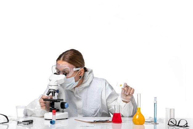 Front view female doctor in protective suit and with mask working with microscope on white background medicine health pandemic virus coronavirus