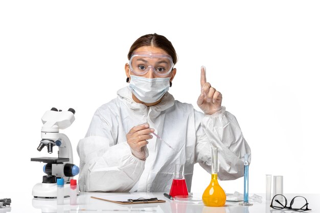 Вид спереди женщина-врач в защитном костюме и с маской, работающая с растворами на светло-белом фоне, пандемический вирус covid, коронавирус