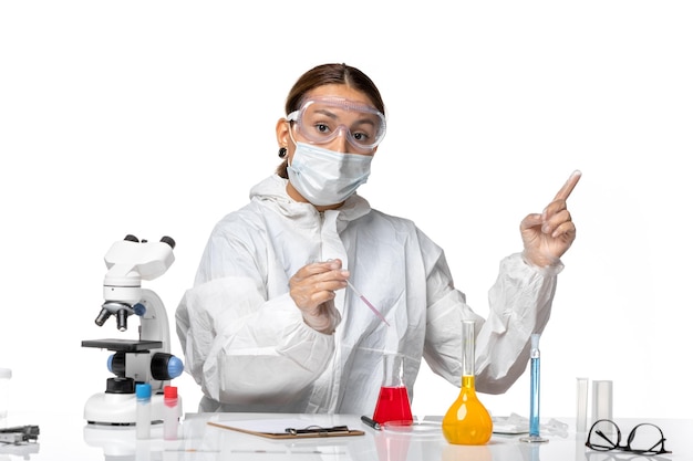 Вид спереди женщина-врач в защитном костюме и с маской, работающая с растворами на светло-белом фоне, пандемический вирус covid, коронавирус