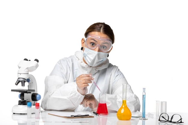 Front view female doctor in protective suit and with mask working with solutions on a white background covid pandemic virus coronavirus