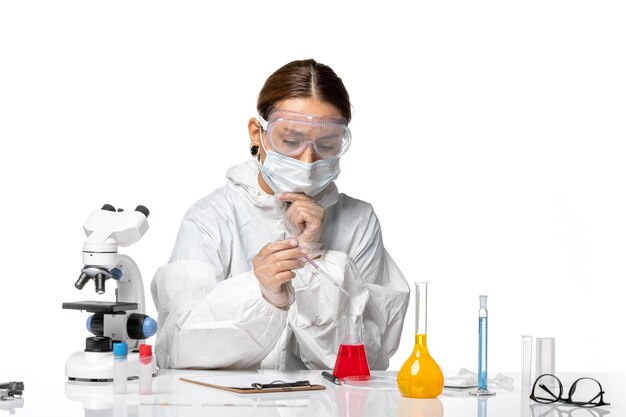 Front view female doctor in protective suit and with mask working with solutions on white background covid pandemic virus coronavirus