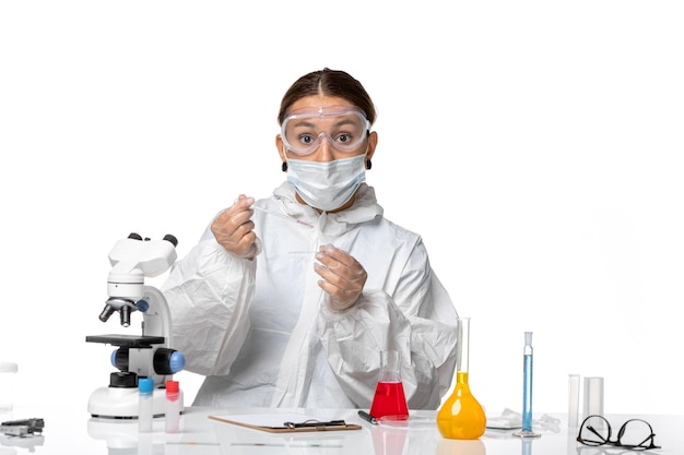 Front view female doctor in protective suit and with mask working with solutions on a white background covid virus pandemic coronavirus