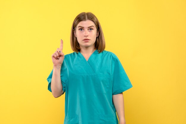 노란색 공간에 그녀의 손가락을 올리는 전면보기 여성 의사