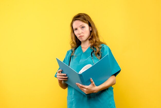 Front view female doctor reading documents on yellow space