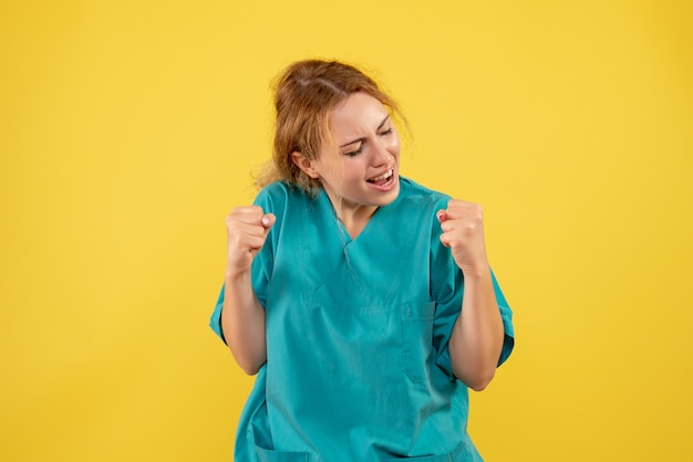 Вид спереди женщины-врача, радующейся в медицинской рубашке на желтой стене