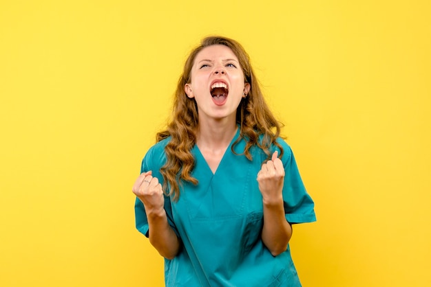 Vista frontale del medico femminile che si rallegra sulla parete gialla