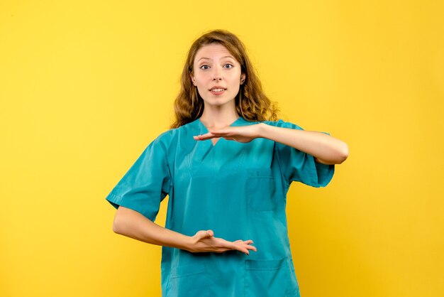 Вид спереди женщины-врача, показывающей размер на желтой стене