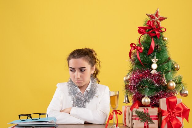 크리스마스 선물 및 노란색 배경에 슬픈 느낌 나무 주위에 앉아 전면보기 여성 의사