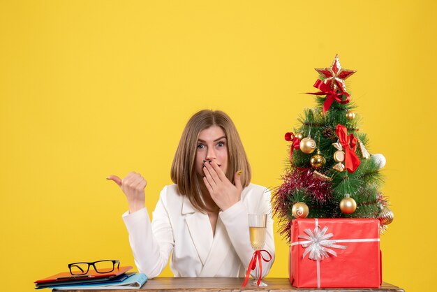 Front view female doctor sitting in front of her table on the yellow background hospital new year christmas health emotion color