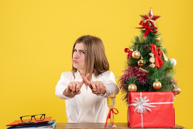 Foto gratuita medico femminile di vista frontale che si siede davanti al suo tavolo su sfondo giallo con albero di natale e scatole regalo