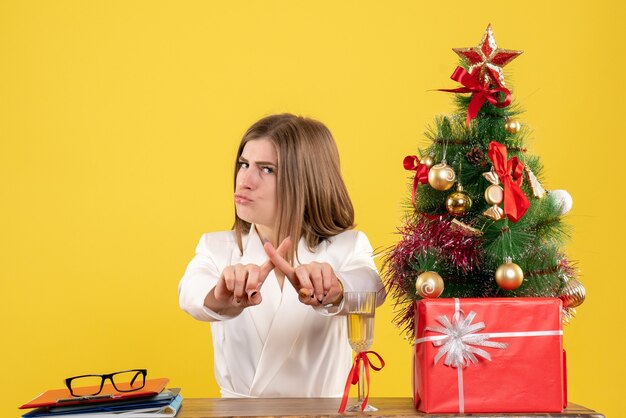 Front view female doctor sitting in front of her table on the yellow background with christmas tree and gift boxes