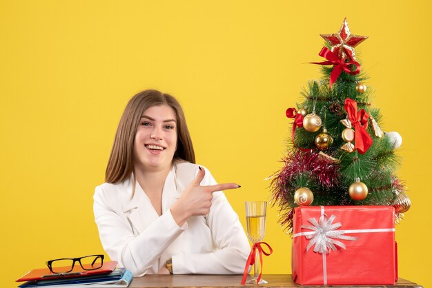 Front view female doctor sitting in front of her table on yellow background