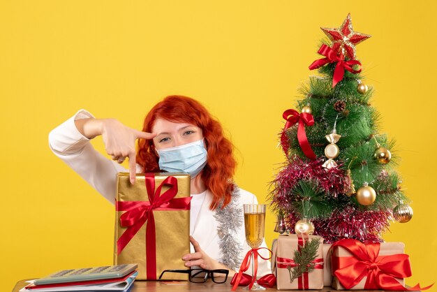 クリスマスツリーとギフトボックスと黄色の背景の木とクリスマスプレゼントとマスクに座っている正面図