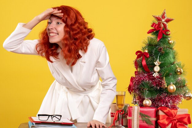 Front view female doctor sitting behind table with christmas presents on yellow background