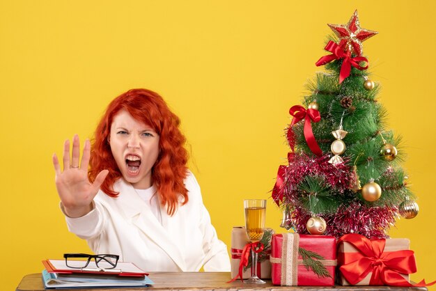 Front view female doctor sitting behind table with christmas presents on yellow background