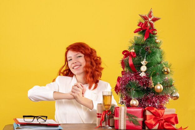 크리스마스 테이블 뒤에 앉아 전면보기 여성 의사 노란색 배경에 선물