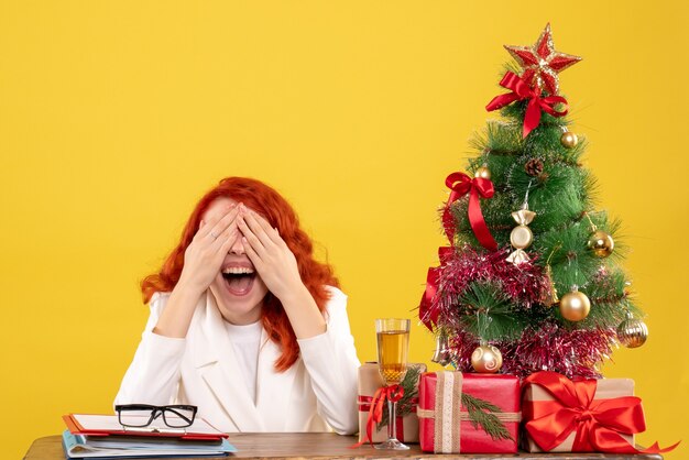 Front view female doctor sitting behind table with christmas presents on yellow desk
