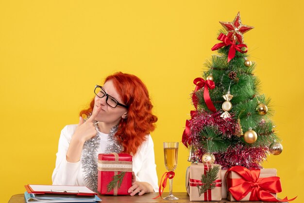 Front view female doctor sitting behind table with christmas presents on yellow