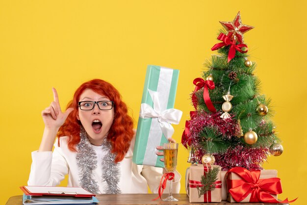 크리스마스 선물 및 노란색 배경에 나무에 앉아 전면보기 여성 의사
