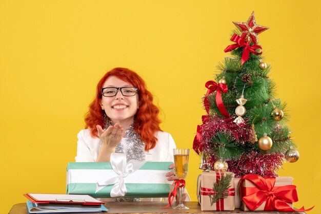 크리스마스 선물 및 노란색 배경에 나무에 앉아 전면보기 여성 의사