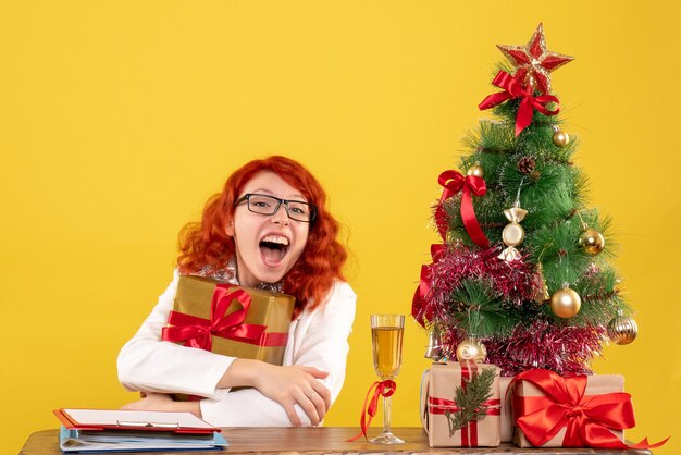 Front view female doctor sitting with christmas presents on yellow background