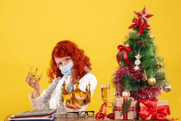 크리스마스 선물에 앉아 노란색 배경에 크라운을 들고 전면보기 여성 의사