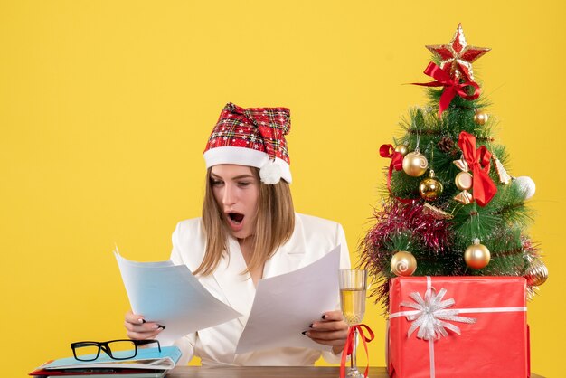 Front view female doctor sitting with xmas presents holding documents on the yellow background