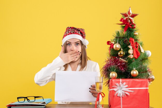 Front view female doctor sitting with xmas presents holding documents on yellow background