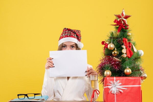 Front view female doctor sitting with xmas presents holding documents on yellow background