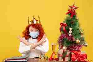 Free photo front view female doctor sitting with xmas presents and wearing crown on a yellow background